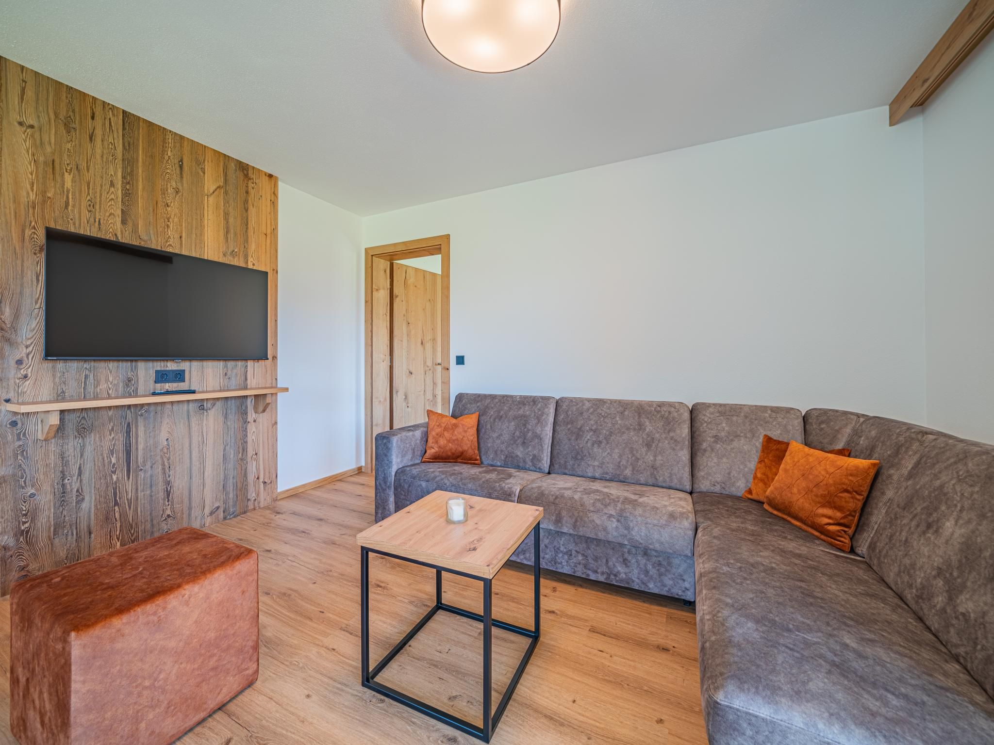 Una sala moderna con un sofá modular, una mesa de centro y un televisor de pantalla plana montado en una pared de madera.