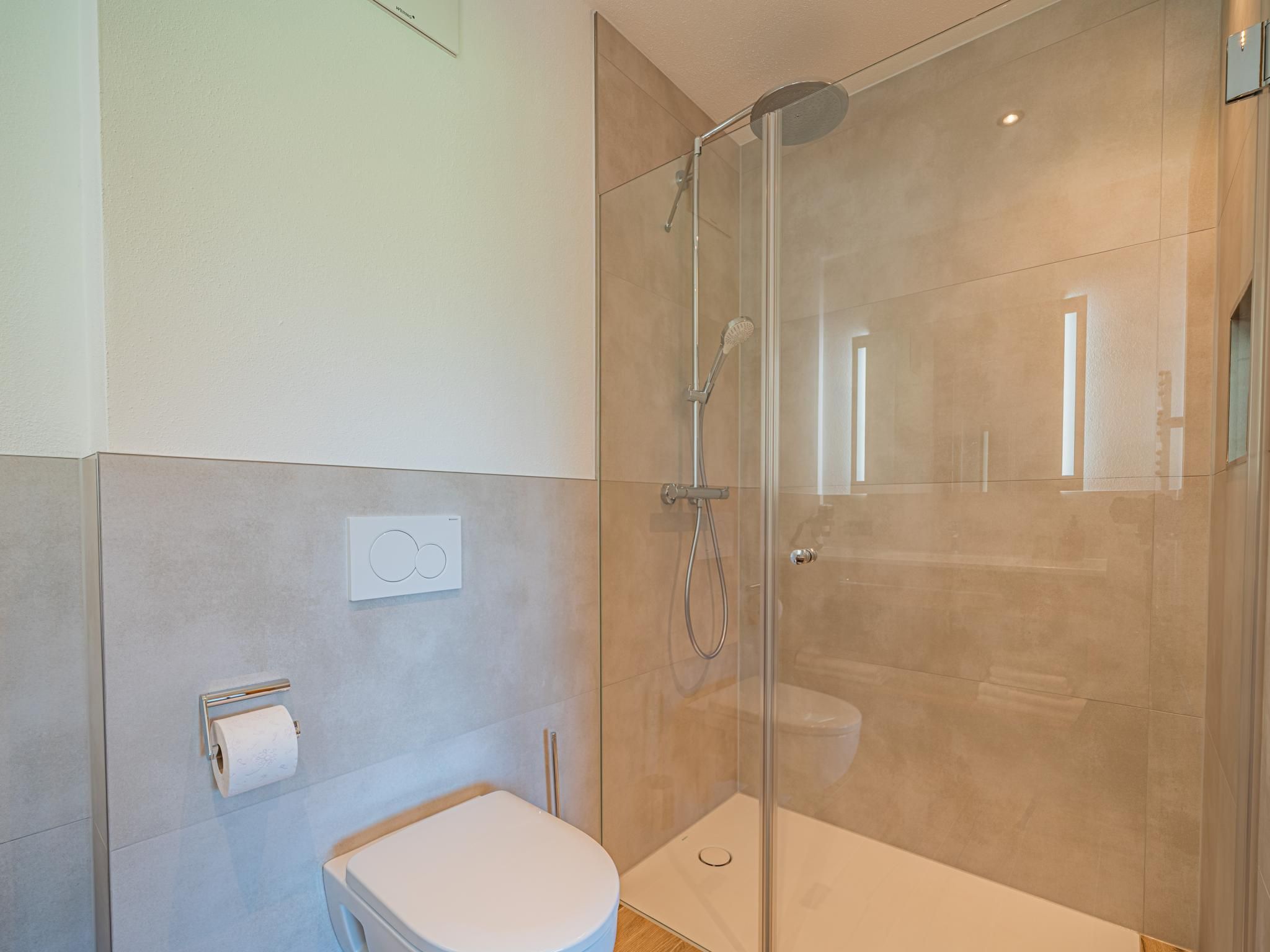 Ein modernes Badezimmer mit einer gläsernen Dusche, einer Toilette und einem wandmontierten Toilettenpapierhalter.