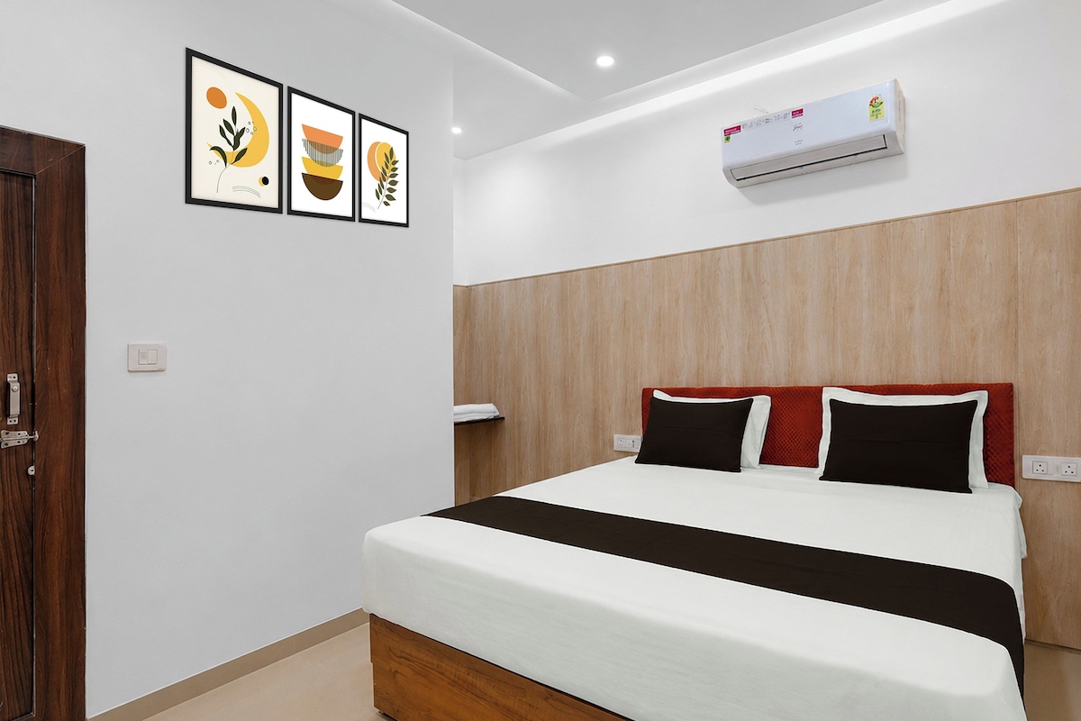 Una habitación de hotel con una cama, cabecera de madera, aire acondicionado de pared y tres cuadros enmarcados.