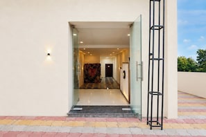Entrada de hotel con puerta de vidrio, piso a cuadros y barandilla metálica a la derecha.