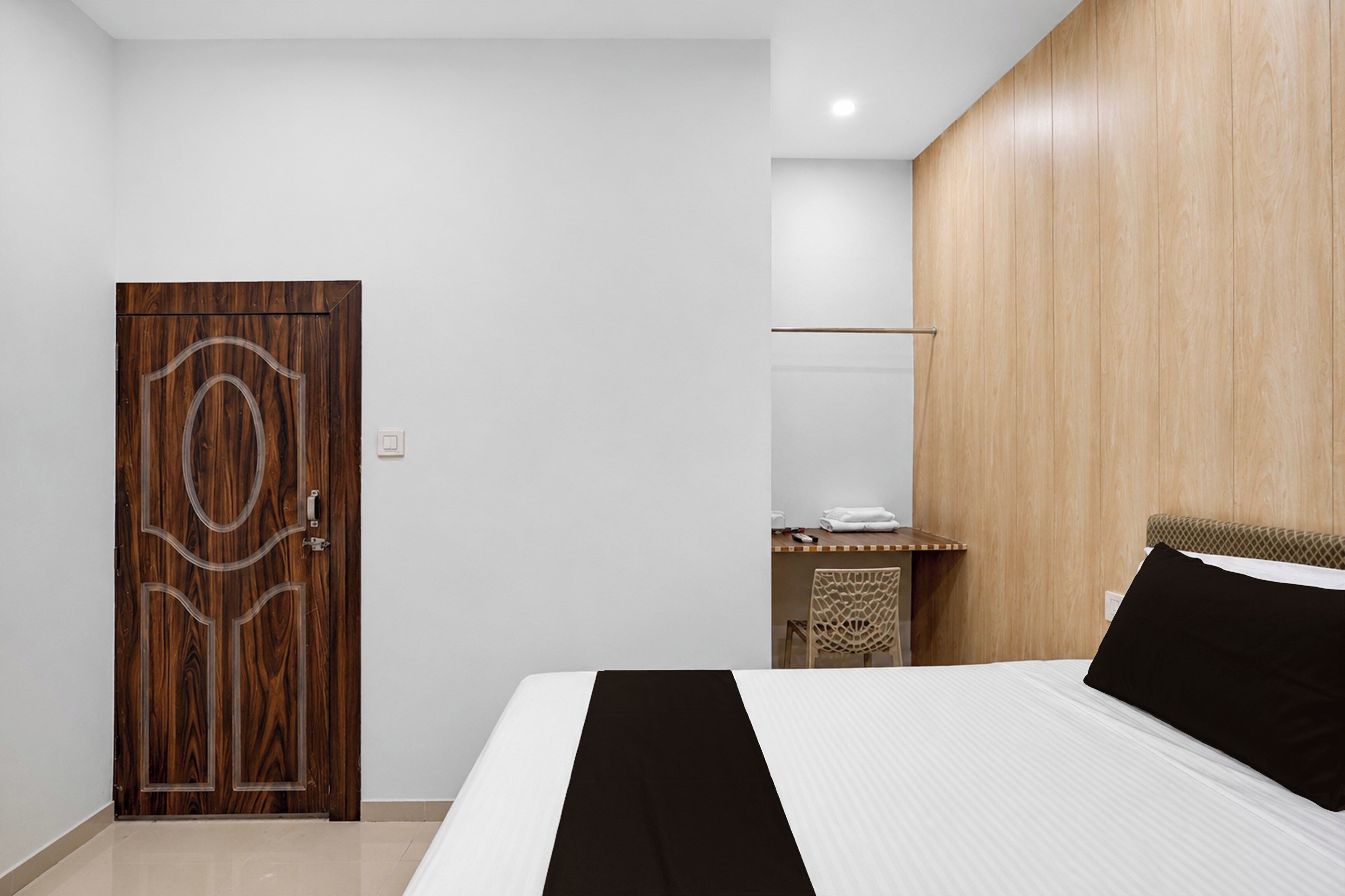 A bedroom with a wooden door, a bed with a black headboard, and a wooden wall panel.