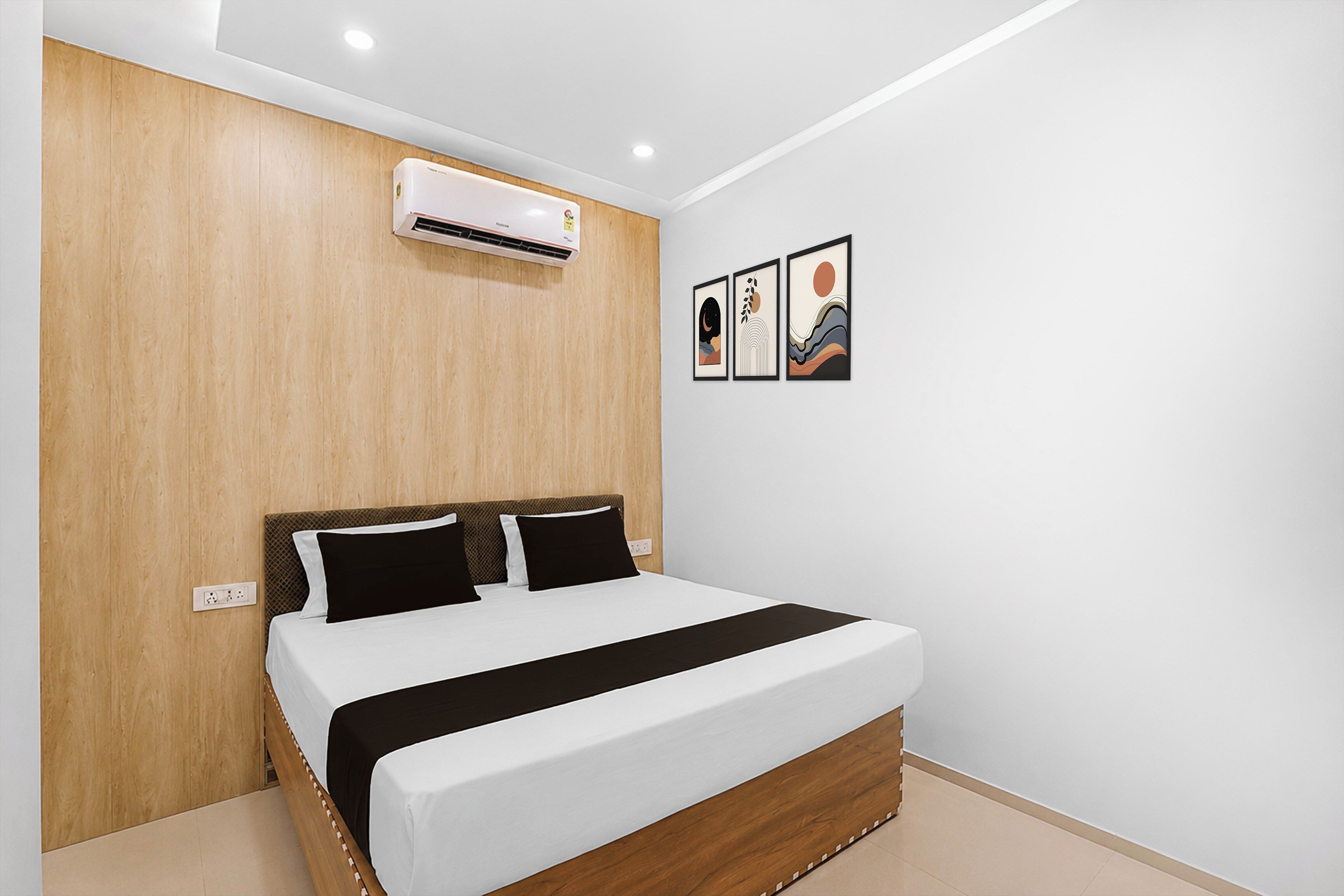 Une chambre à coucher avec une tête de lit en bois, un lit avec une literie noire et blanche, un climatiseur et trois œuvres d’art encadrées accrochées au mur.