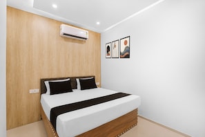 Ein Schlafzimmer mit einem hölzernen Kopfende, einem Bett mit schwarz-weißer Bettwäsche, einer Klimaanlage und drei gerahmten Kunstwerken an der Wand.