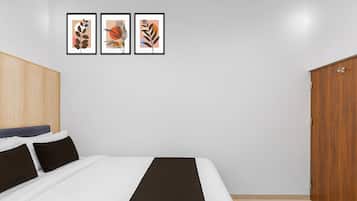 A bedroom with a bed, pillows, a wooden wardrobe, and three framed artworks on the wall.