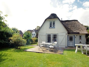 Ein Haus mit Strohdach, einem umzäunten Garten und einer Terrasse mit Gartenmöbeln.