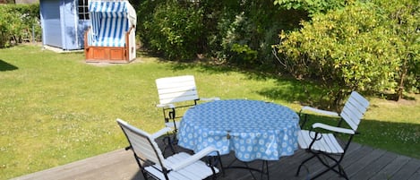 Een terras met een ronde tafel en vier stoelen, omringd door een gazon en een kleine schuur.