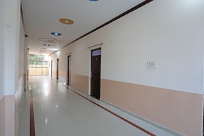Um corredor comprido e estreito, com portas de um lado e uma janela no final.