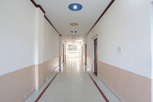 Um corredor comprido e estreito com chão de azulejos, portas em ambos os lados e iluminação embutida no teto.