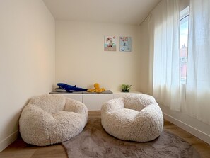 A room with two round, plush seating areas, a small table with a blue object and a yellow plush toy, and a window with curtains. - Stylish stay near the harbor and beach (Blankenberge)