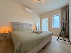 A bedroom with a bed, bedside lamp, air conditioning unit, and a window with curtains. - Stylish stay near the harbor and beach (Blankenberge)