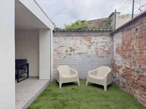Een klein buitengebied met twee witte plastic stoelen, een bakstenen muur en een betegelde vloer.