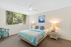 A bedroom with a bed, two bedside lamps, a ceiling fan, a window with a view of greenery, and a painting on the wall. - 3 Bedroom Premium Apartment with Spectacular Views (Gold Coast)