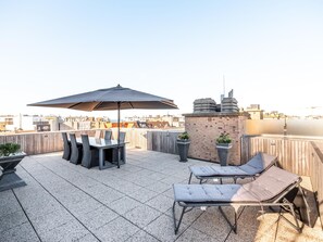 A rooftop terrace with a table and chairs, a lounge chair, and a potted plant. - Bright penthouse with roof terrace near the sea (Koksijde)
