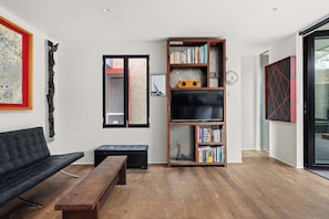 A modern living room with a black sofa, a wooden bench, a bookshelf, and a television. - The Curious Nook - Balaclava Stay (Balaclava)