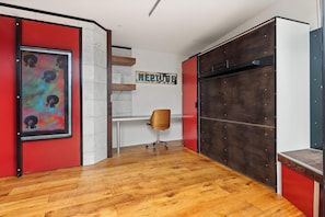 A room with a wooden floor, a desk with a chair, a red door, and a wall with a 'NEPTUNE' sign. - The Curious Nook - Balaclava Stay (Balaclava)