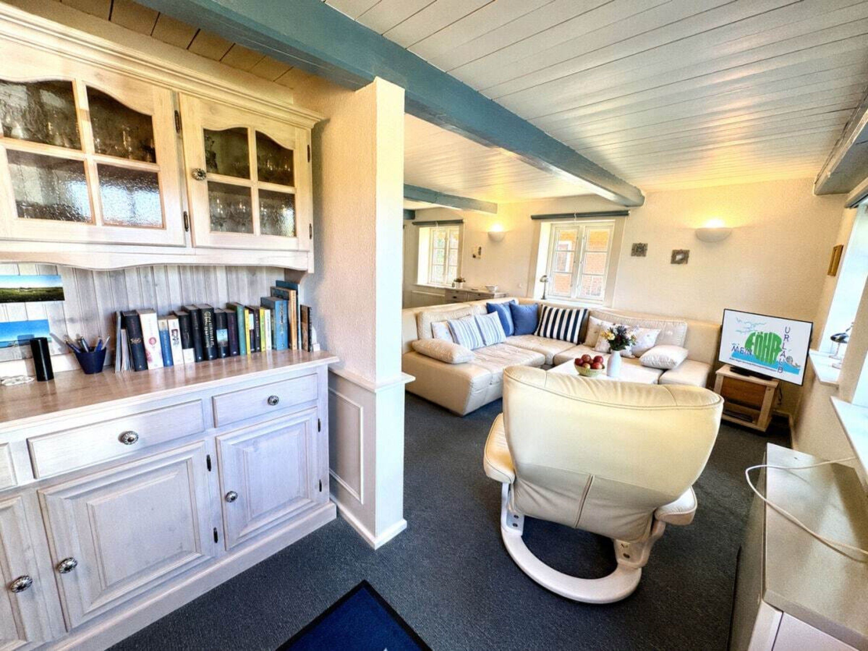 Un salon avec un canapé en cuir blanc, un fauteuil blanc, un téléviseur et une bibliothèque.