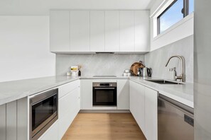A modern kitchen with white cabinetry, a built-in oven, a dishwasher, and a stainless steel sink. - Scenic Rise Beach House at the Bay (Apollo Bay)