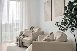 Ein Wohnzimmer mit einer Couch, einem Couchtisch und einem großen Fenster mit durchsichtigen Vorhängen.