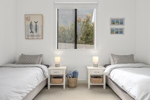 Ein Schlafzimmer mit zwei Betten, einem Fenster mit Jalousien, Nachttischen mit Lampen und Wandbildern.