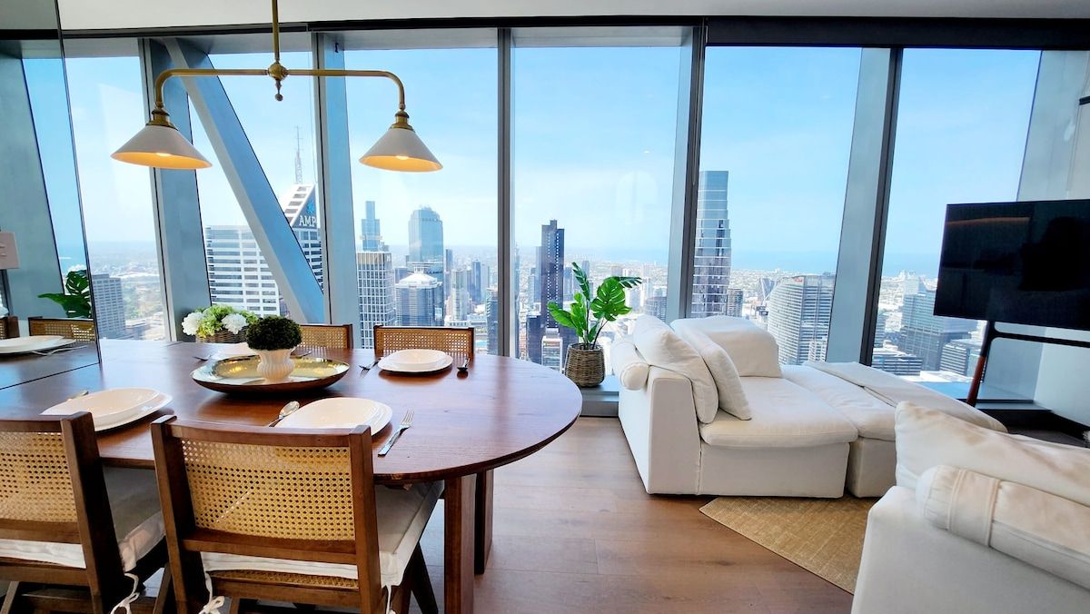 Een moderne woonkamer met een eethoek, grote ramen met uitzicht op de stad en een flatscreen televisie.