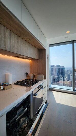 A modern kitchen with a built-in oven and a view of the city through large windows. - Luxury Panoramic Views - 2B2B Pool, Gym & Parking (Melbourne)