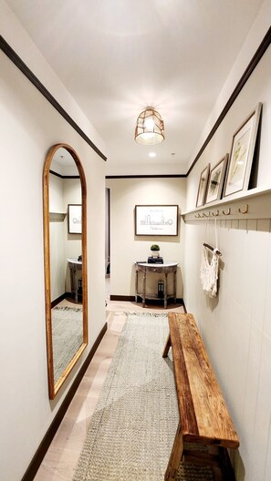 A hallway with a large mirror, a wooden bench, a rug, a wall-mounted light fixture, and framed artwork. - Luxury Panoramic Views - 2B2B Pool, Gym & Parking (Melbourne)