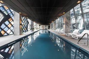 An indoor swimming pool with a long, narrow design, surrounded by lounge chairs and large windows. - Luxury Panoramic Views - 2B2B Pool, Gym & Parking (Melbourne)