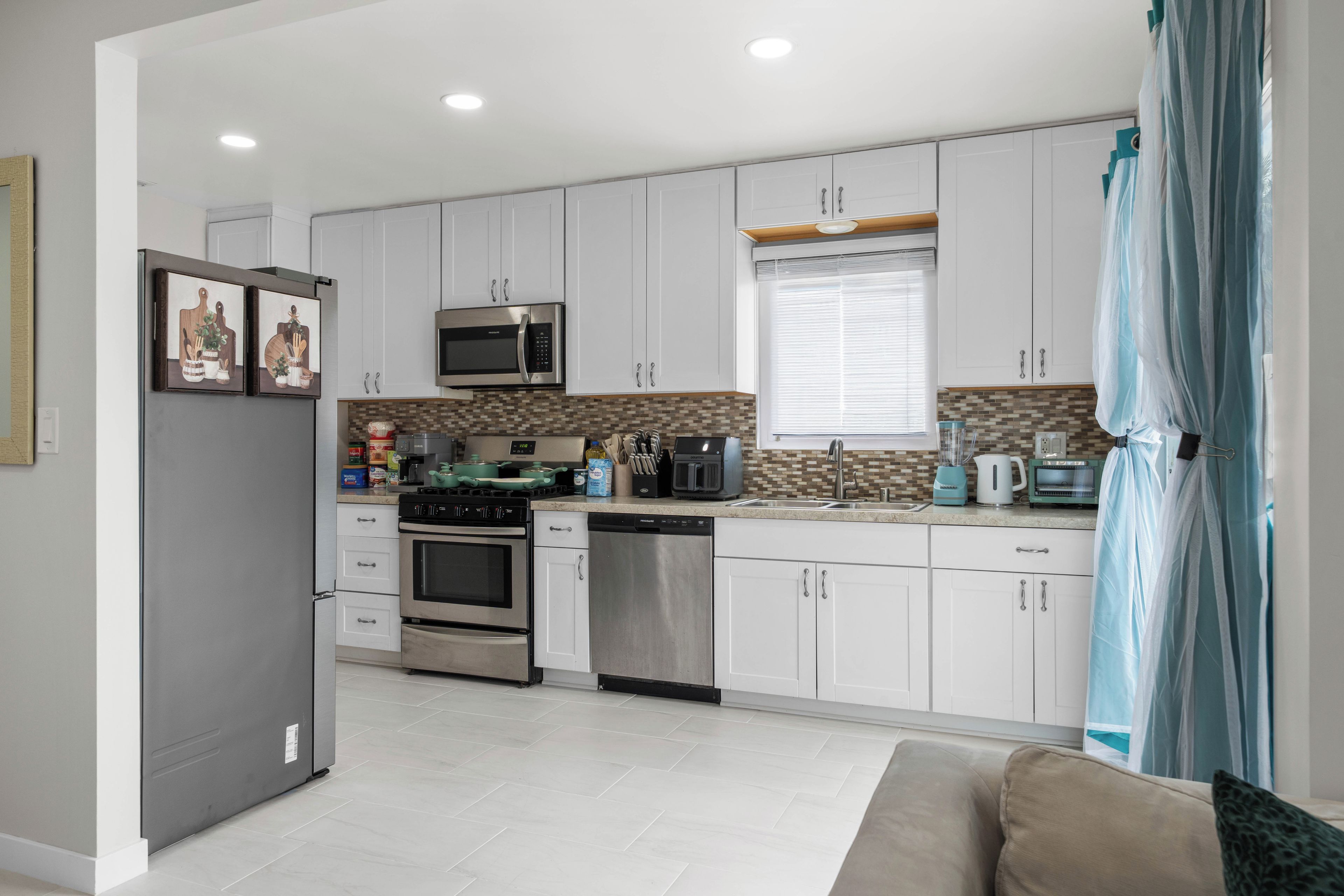 A modern kitchen with white cabinets, stainless steel appliances, and a herringbone tile backsplash.