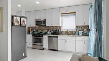 A modern kitchen with white cabinets, stainless steel appliances, and a herringbone tile backsplash.