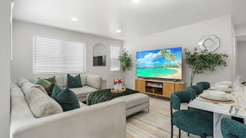 A modern living room with a sofa, TV, dining table, and chairs.