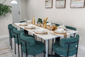 Ein Esstisch ist mit weißen Tellern, goldenen Akzenten und mit grün gepolsterten Stühlen gedeckt.