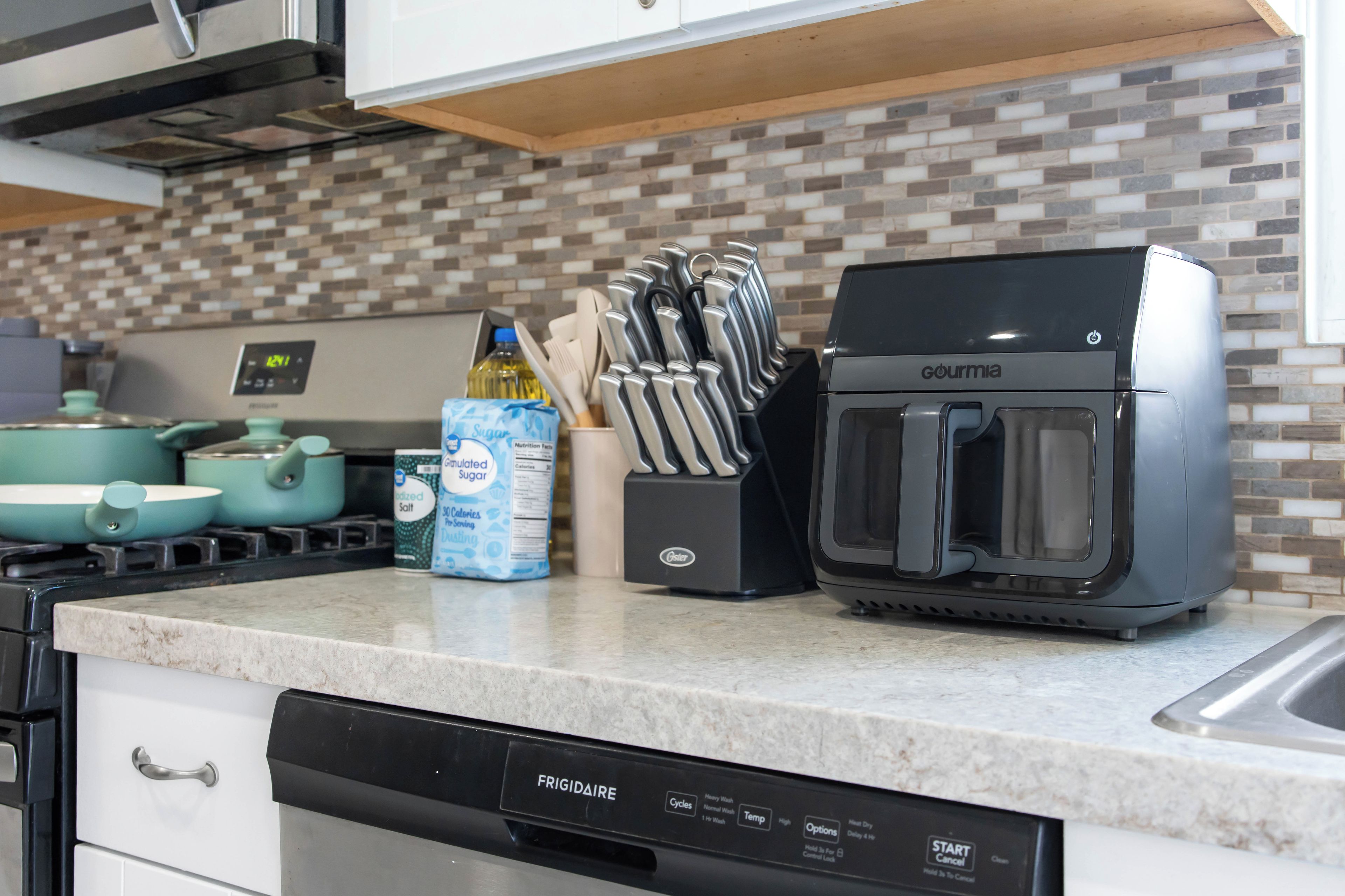 A kitchen with a black coffee machine, a set of knives, a teapot, and a dish soap bottle on the counter.