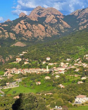 A mountainous town with buildings scattered across the hillside, a prominent church with a bell tower, and rocky peaks in the background. - New Listing (Aubessagne)