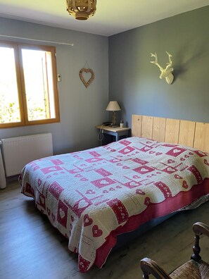 A bedroom with a bed, a nightstand, a lamp, a radiator, a window, and a wall-mounted deer head decoration. - New Listing (Aubessagne)