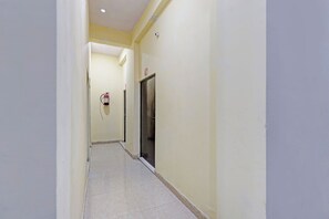 A narrow hallway with a fire extinguisher mounted on the wall, a door with a number sign, and a tiled floor.