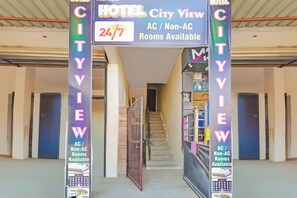 Entrada de hotel com placa indicando quartos com vista para a cidade, disponibilidade 24 horas por dia e opções com ou sem ar condicionado.