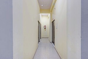 Um corredor estreito com extintor fixado na parede, portas de ambos os lados e chão em azulejo.