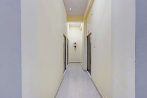 Un pasillo estrecho con un extintor fijado en la pared, puertas a ambos lados y suelo de baldosas.