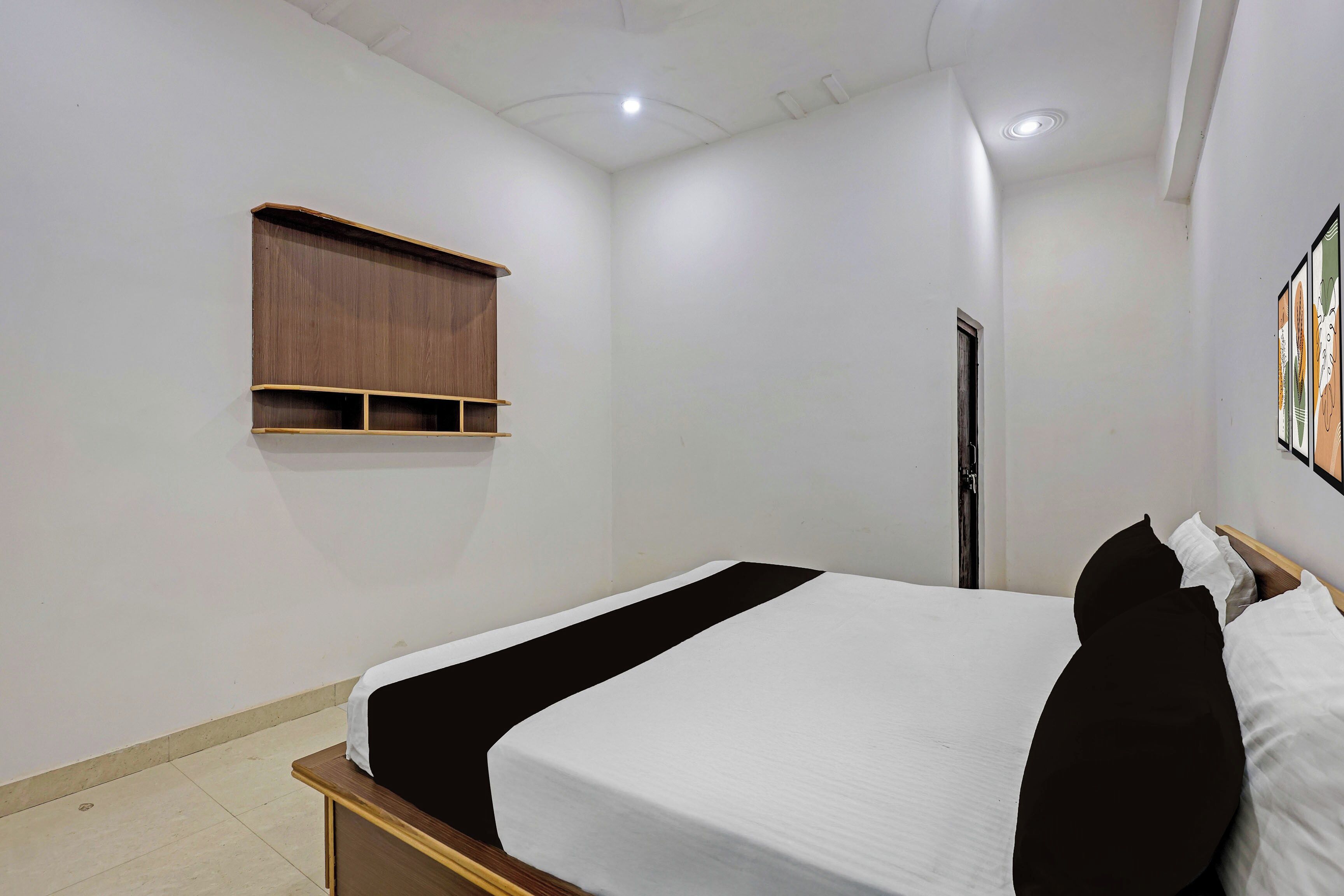 A bedroom with a single bed, a wooden shelf, a door, and a wall-mounted artwork.