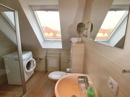 Baño compacto con lavadora, inodoro y lavamanos, con tragaluces y vistas a edificios.