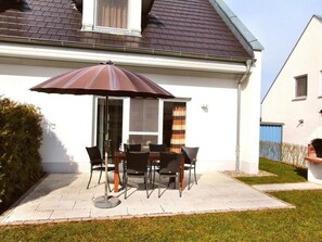 Eine Terrasse mit Tisch und Stühlen, einem großen Sonnenschirm und einem Haus mit geneigtem Dach.
