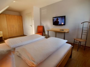 Ein Hotelzimmer mit zwei Betten, einem Fernseher, einem Schreibtisch, einem Stuhl und einem Kleiderschrank.