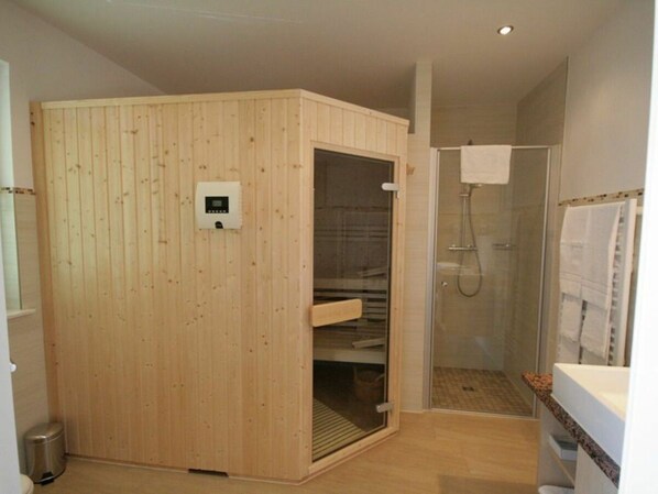 Una sauna con panel de control, ducha envuelta en vidrio y una toalla blanca colgada en la pared.