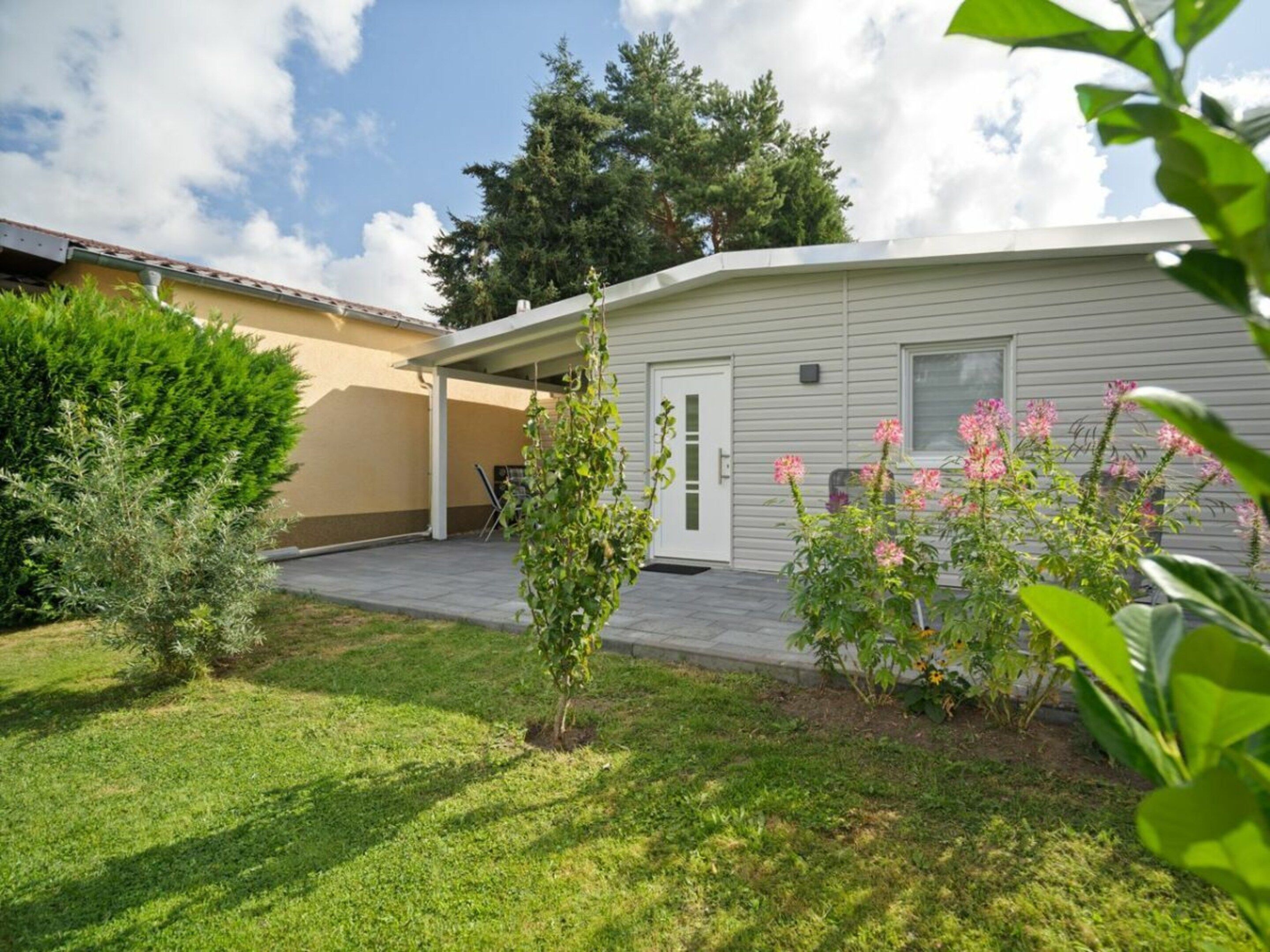 A single-story house with a covered patio, a small garden with flowering plants, and a lawn.