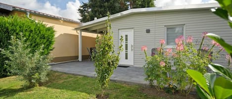 A single-story house with a covered patio, a small garden with flowering plants, and a lawn.