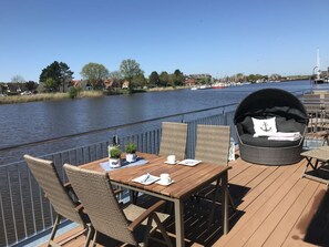 A deck with a table and chairs, overlooking a river with boats and buildings in the background. - Sea Pearl Skartje (Wittmund)