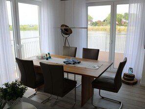 A dining area with a wooden table, four chairs, a laptop, and a view of a body of water through large windows. - Sea Pearl Skartje (Wittmund)