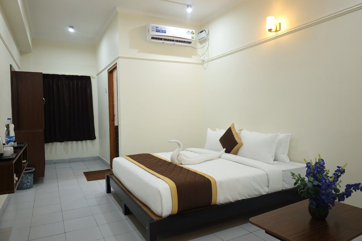 A hotel room with a bed, a desk, an air conditioning unit, and a vase with flowers.