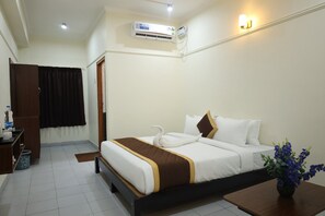 A hotel room with a bed, a desk, an air conditioning unit, and a vase with flowers. - The Golden Park (Dindigul)