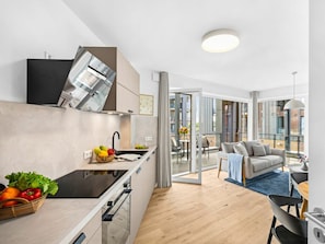 Eine moderne Küche mit Einbauofen, ein Essbereich mit Tisch und Stühlen sowie ein Wohnzimmer mit Sofa und einem Balkon mit Aussicht.
